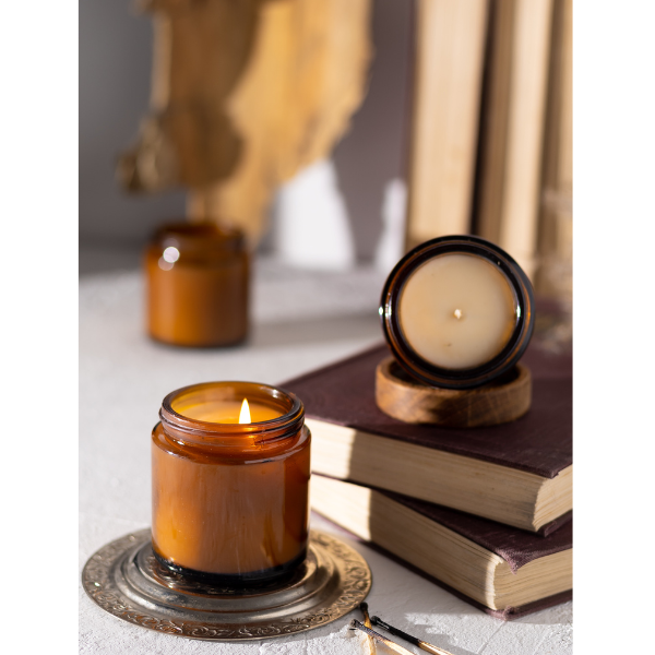 multiple 9 oz soy wax candles in amber glasses sitting on books in a well lit room 