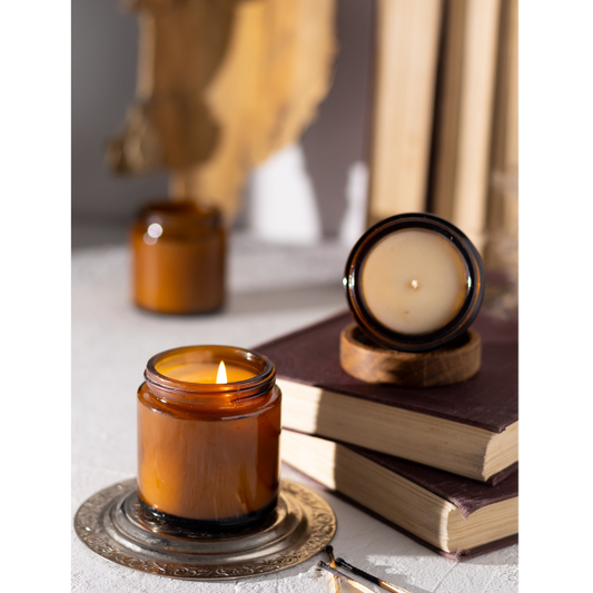 multiple 9 oz soy wax candles in amber glasses sitting on books in a well lit room 