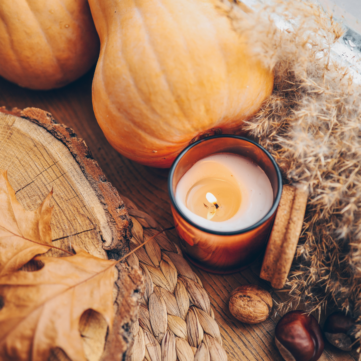 picture fall vibes of burning candle surrounded by orange squash and brown leaves